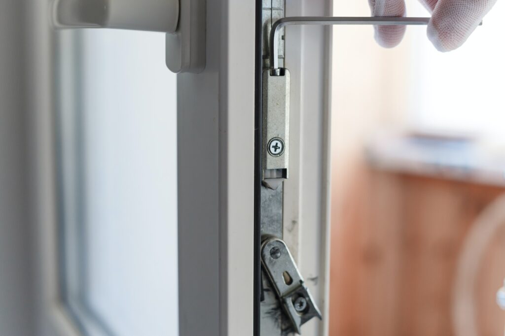 Man's hand makes adjustment of hardware of the uPVC door mechanism with an allen key.